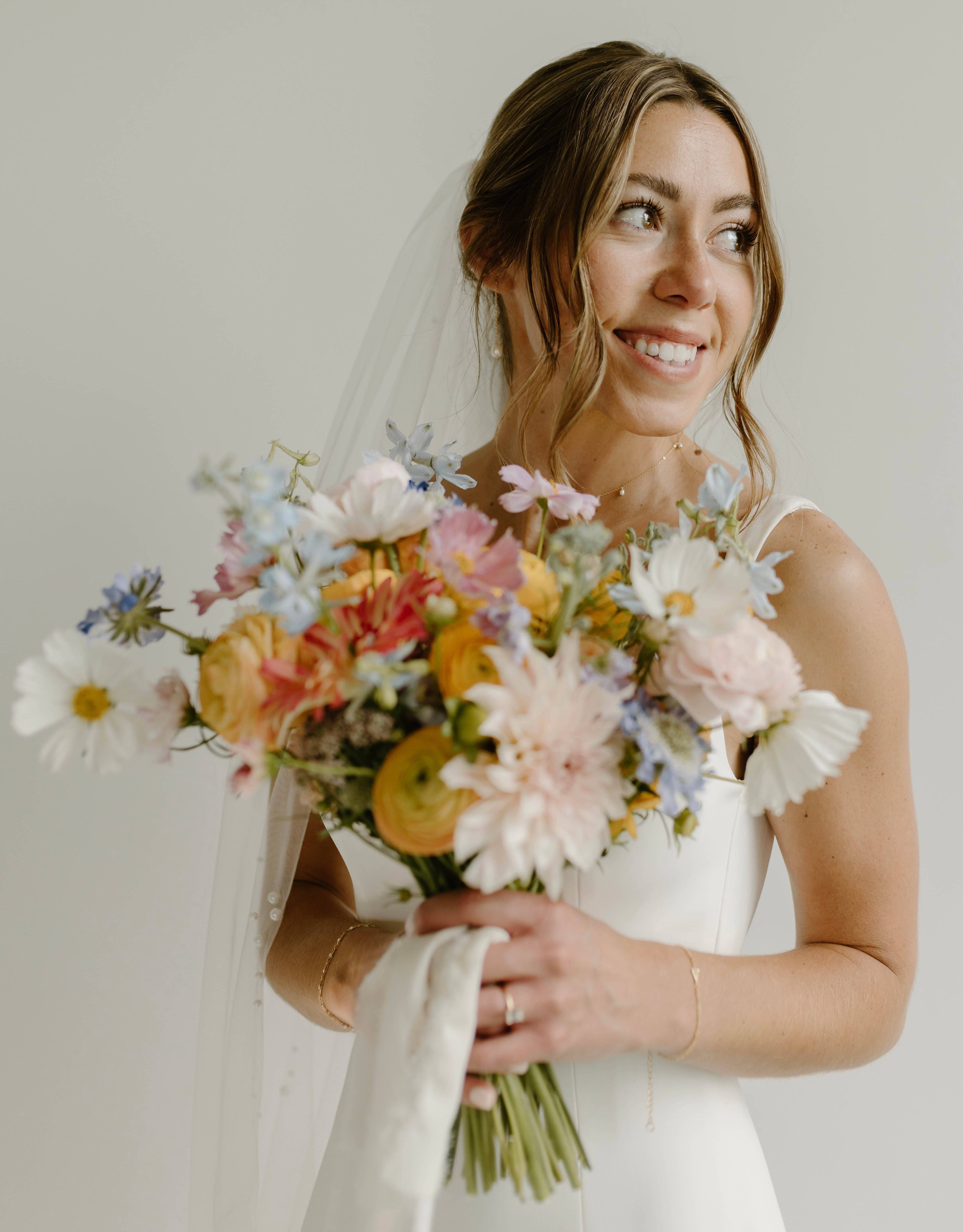 A garden-style hand-tied bouquet was designed for this beautiful bride with florals that included: Dahlia, Cosmos, Ranunculus, Sunflower, and Delphinium wrapped with white silk chiffon ribbon.